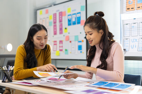 Asian woman designing mobile application layout, discussing creative ideas and teamwork in office meeting.