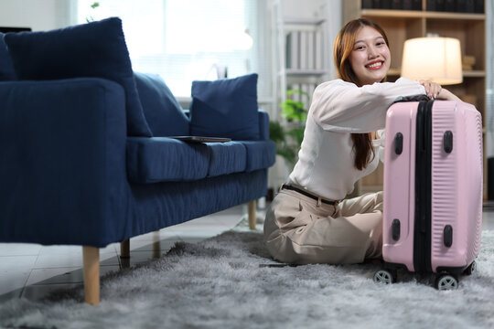 Young woman leaning on pink suitcase, smiling and looking forward to an upcoming trip or holiday. Planning adventure.
