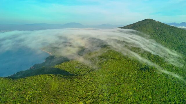 Soft clouds sweep over forested ridges on Son Tra Peninsula near Da Nang, Vietnam, revealing hazy mountains beneath a bright daytime sky
