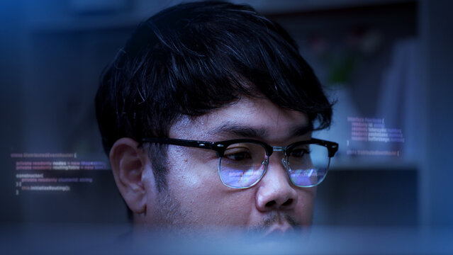 Asian software developer reviewing computer code on monitor with skeptical facial expression and eye reflection in office