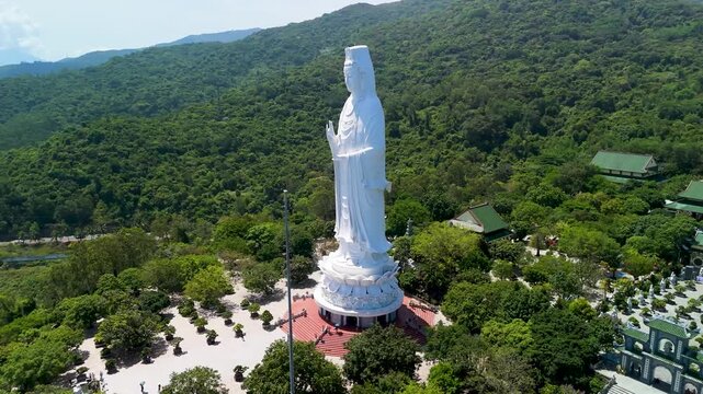 Aerial views circle the towering white Lady Buddha at Linh Ung Pagoda on Son Tra Peninsula, with forested mountains and the sea around Da Nang in daylight