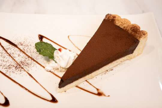 Slice of rich dark chocolate tart dessert served on white plate
