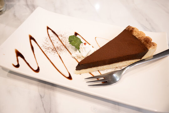 Slice of rich dark chocolate tart dessert served on white plate