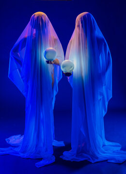 Two ghostly figures holding glowing spheres in blue-lit studio