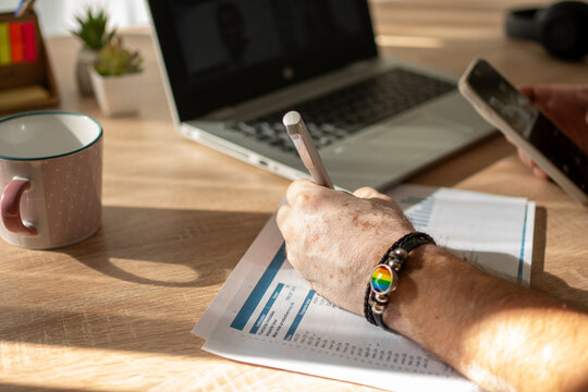 Person uses a smartphone and writes notes beside an open laptop at a desk