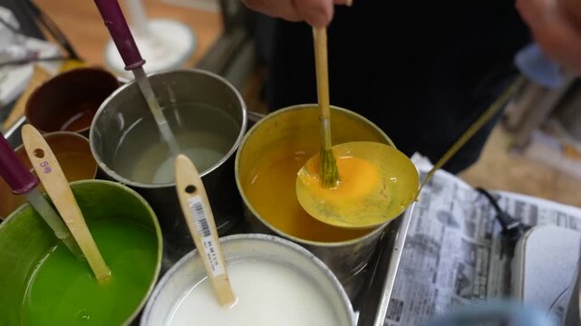 Ladling melted yellow wax from a metal can while preparing replica food