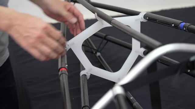 Hands fitting a white rib bulkhead onto the frame of a folding kayak during assembly