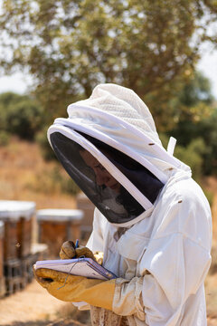 Beekeeper writing notes about honey bee colony at apiary
