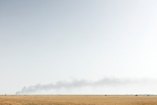 Smoke Plume Across Dry Farmland Horizon Over Flat Field During Distant Fire