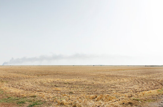 Harvested Field With Distant Smoke Plume on the Horizon Over Flat Rural Landscape at Dry Season