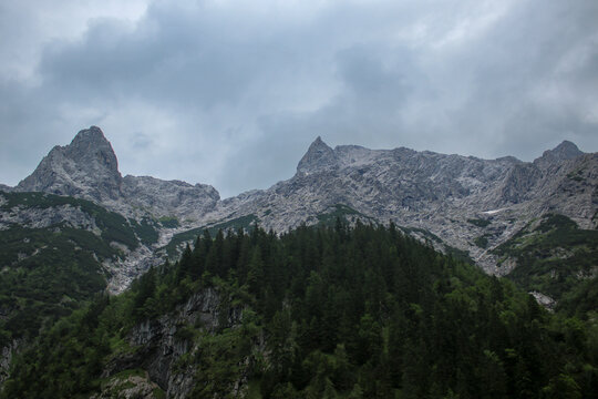 Dramatic rocky mountain peaks above dense pine forest under overcast sky in H&ouml;llental valley near Grainau, Bavarian Alps, Germany. Rugged alpine landscape view near Zugspitze during summer.