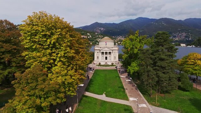 Aerial drone view of Tempio Voltiano in Como, Italy, showcasing the neoclassical museum dedicated to Alessandro Volta, lakeside setting, gardens, and surrounding cityscape.
