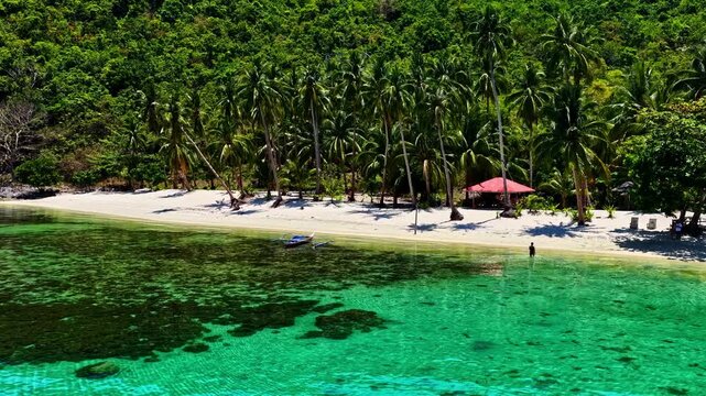 Aerial view of Port Barton Beach with turquoise water, white sand, palm trees, and a person wading in the sea, Mimaropa, Philippines.