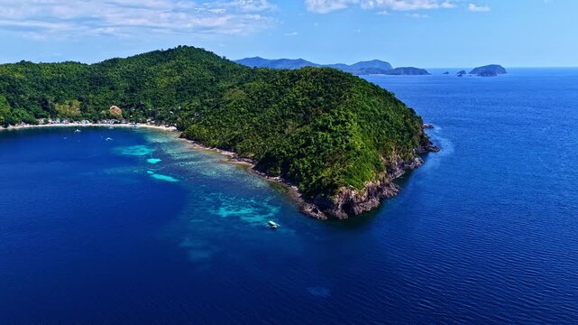 Aerial view of Port Barton Beach with lush green hills, turquoise waters, and a small boat in the ocean in Mimaropa, Philippines.