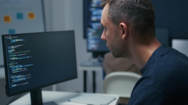 Professional Male Programmer Wearing Glasses Reviewing Source Code and Investigating Technical Problems During Focused Work Session. Programmer Reviewing Computer Code with Concentrated Expression.