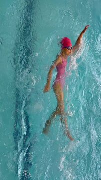 A young girl swimming the backstroke in a clear blue indoor pool. Swimming lessons, childhood sports, aquatic activities