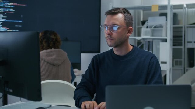 Professional Male Programmer Wearing Glasses Reviewing Source Code and Investigating Technical Problems During Focused Work Session. Programmer Reviewing Computer Code with Concentrated Expression.