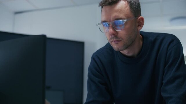 Professional Male Programmer Wearing Glasses Reviewing Source Code and Investigating Technical Problems During Focused Work Session. Programmer Reviewing Computer Code with Concentrated Expression.