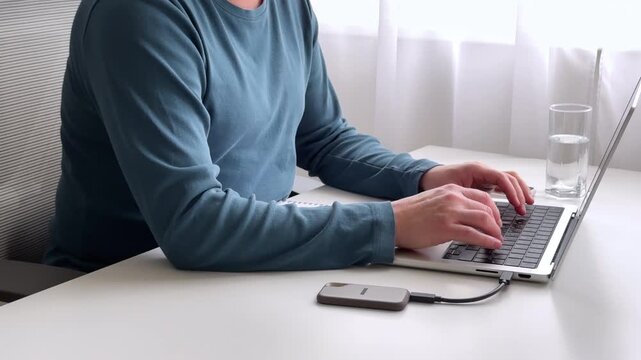 Freelance professional working on computer transferring data to portable SSD at home office. 4K video