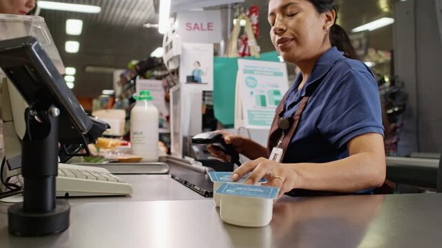 Hispanic young adult woman cashier scanning groceries with barcode scanner at supermarket checkout counter. Suitable for retail commercials and store training videos