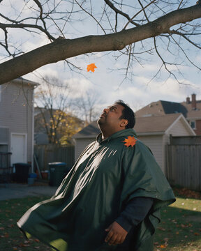 A man in a green windproof poncho looking at a single yellow leaf on a bare branch, embodying the poetic bond of human and autumn nature.