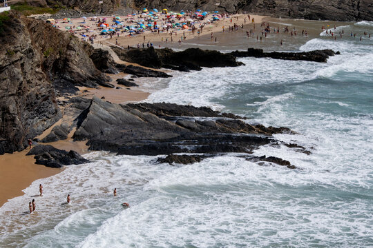 Crowded Coastal Beach Scene with Rocky Outcrops and Turbulent Waves