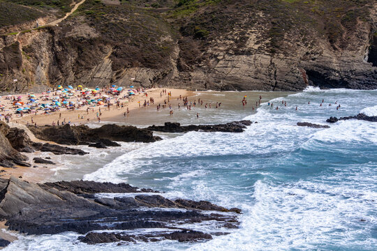 Crowded beach scene with dramatic cliffs and crashing ocean waves