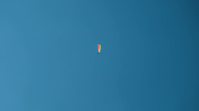 Paragliding clear blue sky adventure with a colorful parachute gliding high in the air. Handheld wide shot of extreme sport activity during a bright sunny day.