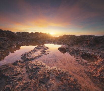 Beautiful rocky sea coast under vibrant sunset sky with long exposure smooth water effect. Twilight ocean shore landscape