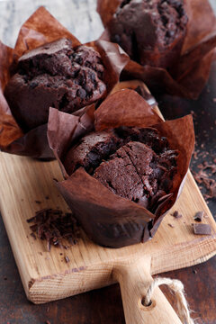 Chocolate muffins in paper wrappers on a wooden cutting board
