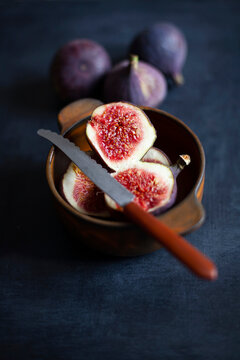 Ripe figs halved and whole in wooden bowl with knife