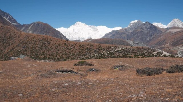Beautiful panoramic view of himalayan mountains with snow covered peaks under clear blue sky. Motion in featuring vast dry valley with sparse vegetation on sunny autumn day to Cho Oyu mountain peak
