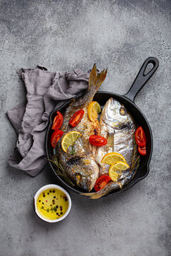 Roasted sea bream with lemon, herbs, and tomatoes in cast iron skillet