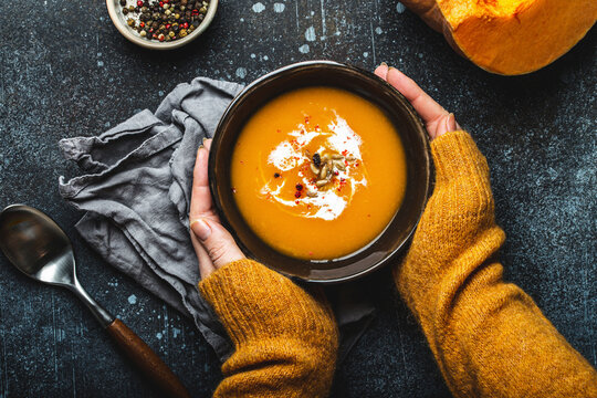 Female hands bowl of pumpkin cream soup garnished with seeds