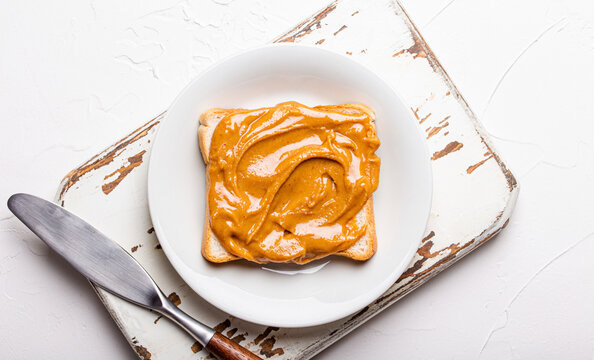 Toast with peanut butter on white plate with knife