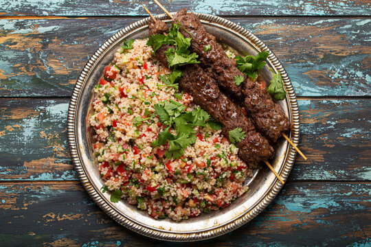 Meat kebab with couscous salad and tabbouleh on rustic table