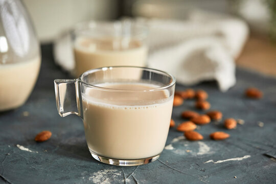 Transparent glass cup and pitcher containing almond milk with whole