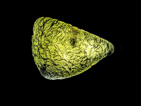 Translucent green Moldavite tektite, backlit on black, revealing its intricate, sculpted extraterrestrial surface