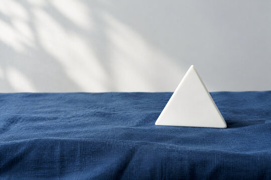 Single white equilateral triangle object on deep blue linen, calm still life for editorial concept