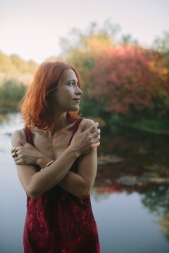 Red haired woman embracing self looking at autumn nature