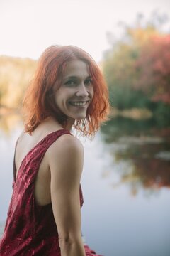 Red haired woman smiling by autumn lake