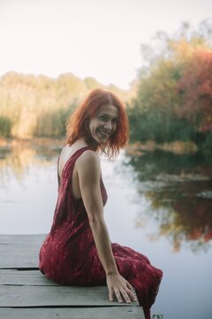 Red-haired woman smiling by autumn lake pier