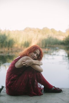 Red haired woman embracing self by autumn lake