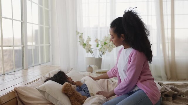 Young mother covers sleepy son with blanket, preparing him for daytime nap