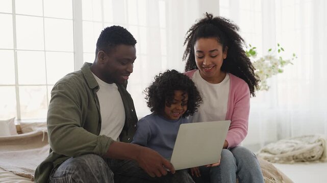 Black parents and little son watch educational video for kids on laptop