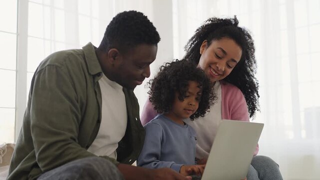 African American parents help little son play educational game on laptop