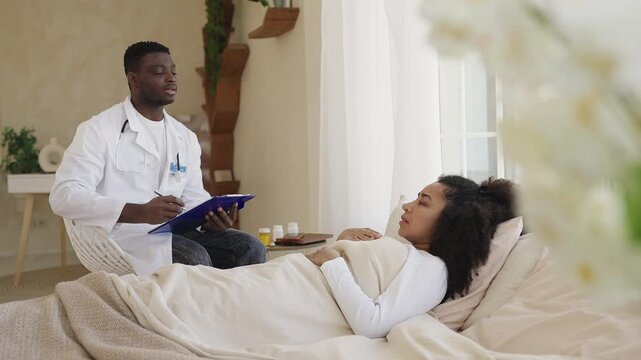African American woman lies in bed and talks with male doctor during home visit