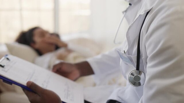 African American male doctor fills out medical form while consulting sick woman