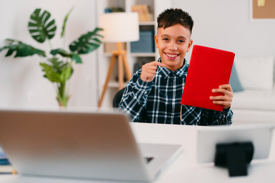 Smiling student pointing at book during online class