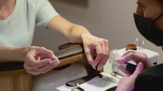 A horizontal video showing a manicurist replacing an attachment bit on an electric nail drill while conversing with a client in a salon.